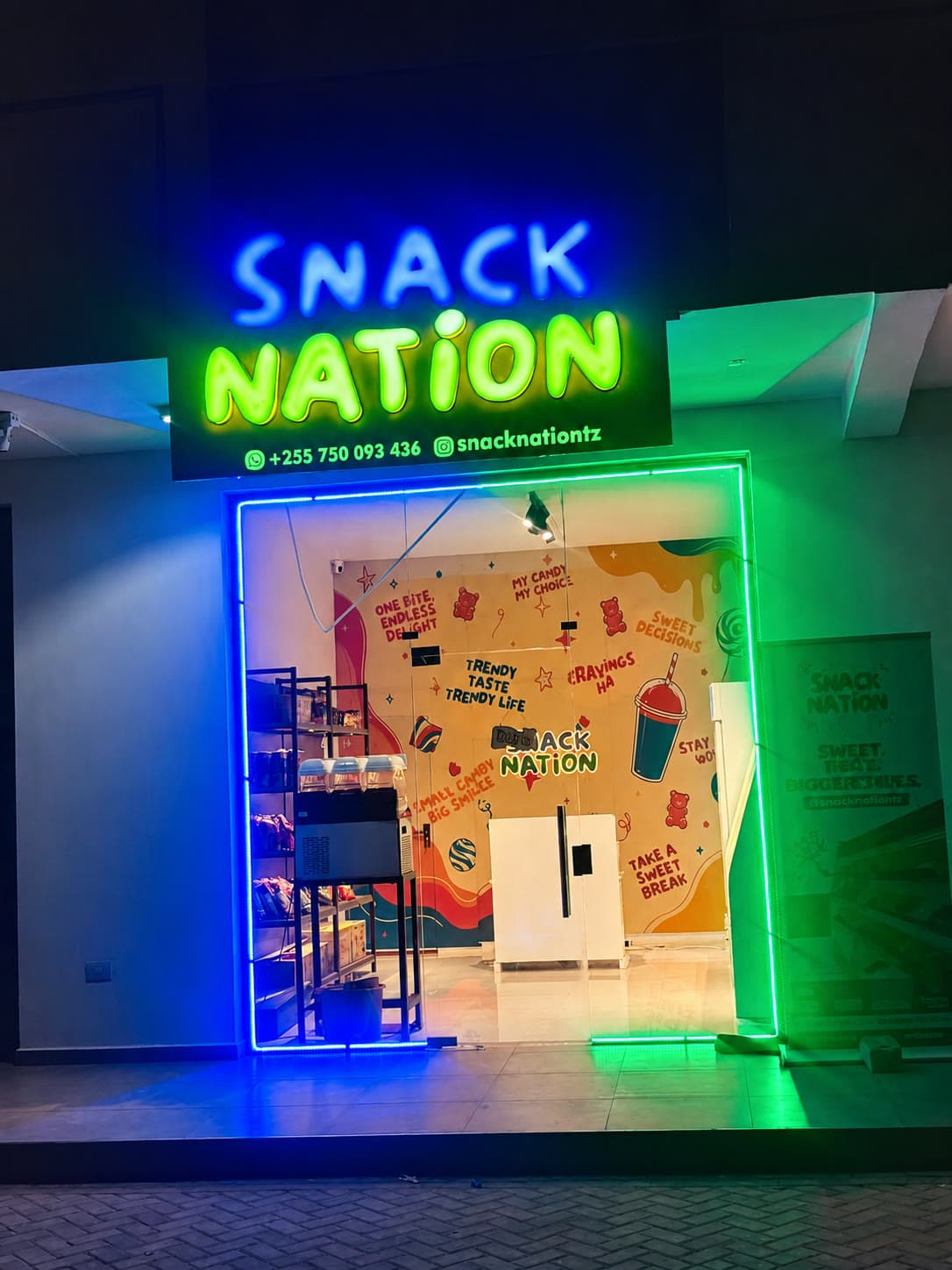 Snack Nation's storefront at night, lit up with blue and green neon signage